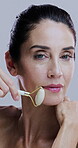 Face, jade roller and wrinkles with mature woman in studio for morning cosmetics or skincare routine. Antiaging, massage and relax with person on white background for dermatology or natural beauty