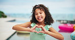 Girl, child and heart hands by swimming pool, smile and excited for memory, playful and vacation. Kid, happy and kindness with sign, emoji and laugh with symbol, summer and holiday in Costa Rica