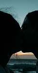 Love, couple and kissing by beach at night for romantic date, anniversary and holiday adventure. Silhouette, sunset and people with affection in nature for relationship, honeymoon vacation and care
