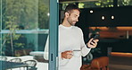 Man, phone and coffee in morning, home and texting by glass door, smile and check notification. Person, smartphone and click on mobile application, tea cup and contact on social network at apartment