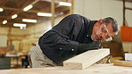 Carpentry, woodwork and man in workshop with dust on wood for furniture, manufacturing and lumber production. Construction, workshop and carpenter blowing for planks, timber and board for renovation