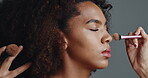 Makeover, hands and woman with makeup, brush or preparation of model with foundation or cosmetics. Studio, artist and tools on person for beauty, grooming or application of product or grey background