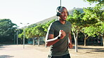 Headphones, running and black man in park for training, wellness and fitness. Radio, podcast and African athlete with endurance exercise, challenge and workout for cardio and jog outdoors in nature