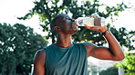 Black man, fitness and drinking with water bottle at park for hydration, break or rest in nature. Active, thirsty or male person with mineral liquid for workout, exercise or natural sustainability