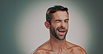 Skincare, face and man with wink in studio for glow, natural and morning treatment. Cosmetic, hygiene and portrait of male person with facial, dermatology or grooming routine by gray background.