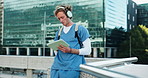 Headphones, doctor and student with tablet outdoor studying for clinical exam or test. Education, technology and female healthcare intern listening to music and reading online textbook in city.
