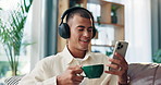 Cellphone, coffee and man with headphones on sofa in morning watching funny online video in home. Laughing, relax and male person in living room with cappuccino, phone and audio tech for streaming.