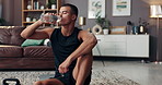 Tired, fitness and drinking water with man in living room for exercise, hydration and health. Workout, wellness and resting with person on floor of home gym for sports, bodybuilder and thirsty