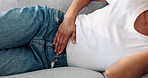 Home, hands and woman on couch, period pain and gut health with constipation in living room. Closeup, apartment and person with menstruation, pms and digestion with health risk and menstrual cycle