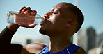 Black man, runner and drinking water in city on break, training and tired with hydration for wellness in summer. Person, bottle and liquid for workout, exercise and fitness for marathon in Cape Town