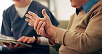 Caregiver, hand and senior person with arthritis, nursing home and numbness of fingers in lounge or pain. Retirement, closeup and pensioner with carpal tunnel syndrome, helping and nurse with tablet