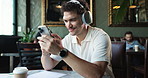 Headphones, music and man in coffee shop with phone listening to song, radio and playlist. Restaurant, happy and person on smartphone for internet, streaming and audio subscription on break in cafe