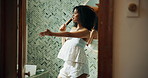 Woman, hairbrush and singing in home, bathroom and concert by mirror, playful and voice in morning with smile. Person, hair care and happy with karaoke, reflection and funny performance at apartment