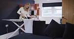 Ironing, chores and woman working on laundry on a board in the living room of a house. Cleaning, housekeeping and housewife with an iron for clean clothes, tidying and doing housework in a home