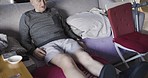 Senior man, leg pain and rehabilitation in home after fall or accident. Help, physiotherapy or elderly retired man talking in living room on sofa with sore legs, joint or muscle inflammation in house