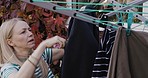 Laundry, clothes and hanging washing on clothesline by a mature woman at home in the garden. A lady doing chores, cleaning and drying wet, clean clothing on a line, outdoor in her backyard
