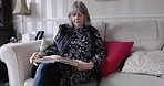 Relax, book and senior woman reading a fantasy novel while sitting on a sofa in her living room. Calm, peace and elderly lady in retirement enjoying a story while relaxing on the couch in her home.