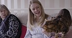 Mother, adult daughter and cat bonding, playing and in communication on the living room sofa of their house. Family, love and woman speaking, giving affection and care to a pet animal with senior mom