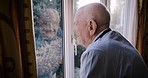 Senior man, thinking and looking out of window, depression and lonely in retirement home, mental health and anxiety. Elderly male, frustrated and depressed in house with grief, alone and sad in room
