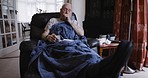 Covid, cough and sick with a senior man in his retirement home keeping warm with a banket on the sofa. Health, pain and allergy with a mature male suffering from the corona virus in his living room