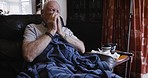 Senior man, sick and cough while on sofa with flu, allergy or covid with a blanket and tissue in retirement. Elderly or old person in New Zealand house with bad health or cold while blowing nose