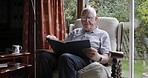 Elderly man, home and reading book, glasses or rocking chair in apartment by window for peace. Senior gentle, focus and sitting to read, learn or rest on sofa in lounge, living room or house to relax