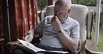 Senior man, reading book and relax on the couch in home with glasses, sofa, calm and peace in living room. Content, retired and elderly male, literature and read novel, story and relaxing on couch