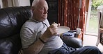 Senior man, food and eating bread while sitting in a chair in his retirement home. Retired elderly male, eat and snack for diet and nutrition or sandwich in his house while hungry and resting
