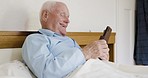 Phone, relax and senior man in bed scrolling on social media, mobile app or the internet at his home. Rest, technology and happy elderly guy relaxing in his bedroom while typing message on smartphone