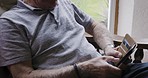 Phone, relax and senior man in a chair scrolling on social media or the internet in the living room. Rest, technology and elderly guy in retirement typing a text message on a smartphone at his home.