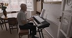 Senior man, piano and reading music notes at home or relaxing, playing keyboard and musician practicing. Pianist, musical instrument or elderly person play music or learning for artistic performance