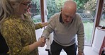 Disability, help and senior couple holding hands for walking, balance and support in their home together. Love, trust and elderly woman helping man in wheelchair, standing and hold hand while bonding