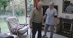 Woman nurse helping a senior man to walk with a stick in the living room of his retirement home. Healthcare, medical and elderly nursing caregiver assisting a male patient with walking in his house.