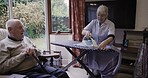 Senior couple, home and communication in living room while doing ironing, cleaning and happy bonding. Old man and woman cleaner, caregiver or nurse in house for clean laundry and talking retirement