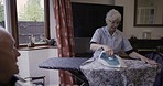 Ironing, clothes and senior couple in discussion during housework, chores and cleaning. Communication, speaking and elderly woman with company from a man during housewife work in the living room