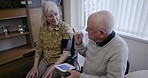 Senior care, blood pressure and couple discussing how to use health measurement machine in living room. Hypertension, reading and elderly woman and man explain instructions for wife with disability