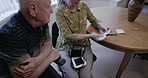Senior care, blood pressure and couple with instructions for health measurement machine in living room. Hypertension, reading and elderly man and woman reading paper note for husband with disability