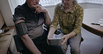 Senior couple, blood pressure and home check for medical test, cholesterol and hypertension. Old people, arm pulse and monitor heart healthcare, diabetes risk and cardiovascular wellness in apartment