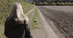 Woman, walking in countryside and relax in nature trekking on farm with freedom and fresh air from back. Peace, farmland and girl hiking in natural landscape enjoying travel sun and green environment