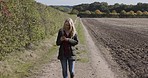 Woman, phone and countryside while walking on farm for connection, communication and location with smile. Happy person with smartphone to check mobile app for weather, field sustainability or ecology