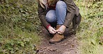 Woman stop, mountain walk and shoes tie of a person on nature path hiking for wellness. Dirt trail, fitness and young person with freedom and travel outdoor feeling calm and relax from green plants