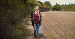 Woman, walking and smile for travel, countryside or adventure on a sunny day in the nature outdoors. Happy blond female smiling in joyful happiness taking a natural walk or stroll outside on a farm