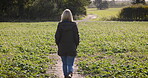 Walking, lonely and calm woman outdoors on a farm, land and nature in the countryside on vacation or holiday. Back view, alone and female farmer on farmland to clear her mind for peace and freedom