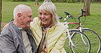 Happy senior couple outdoor and in love, spending quality time together in nature on a bench. Retirement and man and woman enjoy a relax day in a park or garden
