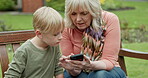 Grandmother, young boy and kid with cellphone on park bench for games, app and social media. Senior woman, grandchild and smartphone in garden for connection, download and reading notification