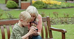 Grandmother, young boy and kid with cellphone on park bench for games, app and social media. Senior woman, grandchild and smartphone in garden for connection, download and reading notification
