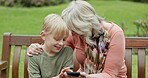 Grandmother, young boy and laughing with cellphone on park bench for games, app and funny meme. Senior woman, grandchild and smartphone in garden for connection, download and reading notification