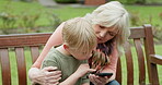 Grandmother, young boy and kid with cellphone on park bench for games, app and social media. Senior woman, grandchild and smartphone in garden for connection, download and reading notification
