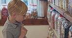 Kid thinking, choice and shopping in a candy store with sweets, confectionery or boy in a retail supermarket, shop and sale of candies. Jar, shelf and child or toddler choosing chocolate product