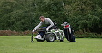 Person with disability, man and ball for golf with tool for tee on grass, lawn and course. Male paragolfer, sitting and wheelchair for practice of sport with competition, tournament or recreation